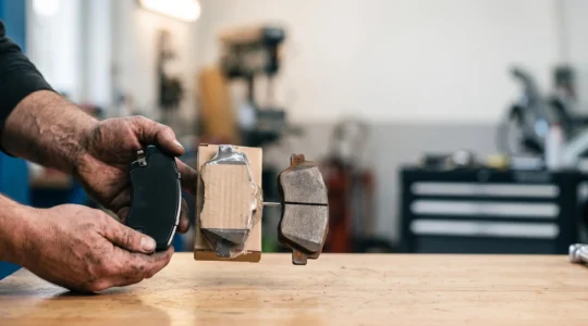 Mécanicien comparant trois pièces automobiles différentes dans un atelier lumineux, symbolisant le choix entre pièce d'origine, adaptable et occasion